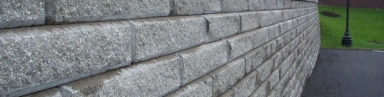 Granite grey retaining wall with a smooth, modern finish, supporting a landscaped garden area